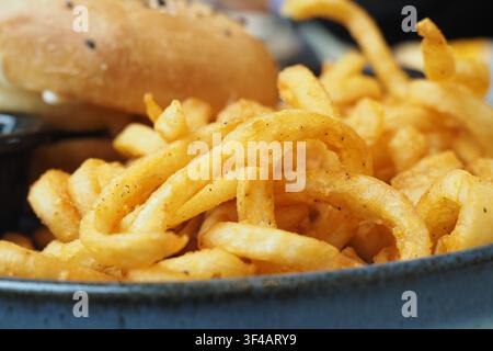 Geschwungene Pommes und Burger serviert auf einem Teller in einem Restaurant Stockfoto