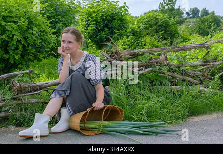 Junge Frau ruht sich nach der Ernte mit frischen grünen Zwiebeln in einem Bio-Garten auf dem Land aus Stockfoto