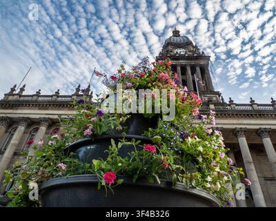 Stufige Blumenurne, die unter der Kuppel und dem Glockenturm des Leeds Town Hall mit rosa und lila Blüten überfüllt ist Stockfoto
