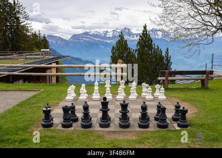 Riesige Schachfiguren, die auf einem Außenschachbrett angeordnet sind, vor einer malerischen Bergkulisse Stockfoto