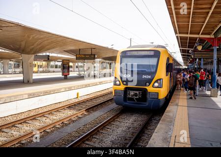 Porto, 17. Juni 2022: Gelber Zug kommt an einem modernen Bahnhof an, Passagiere warten auf dem Bahnsteig. Stockfoto