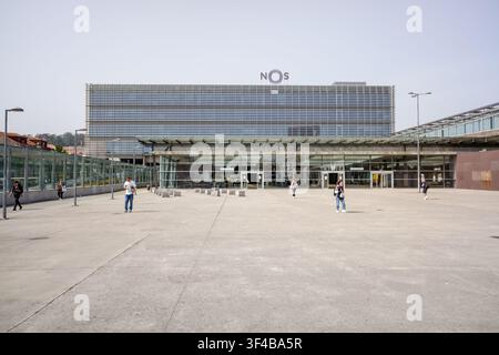 Porto, 17. Juni 2022: Moderne Nos-Baudenkelfassade mit Menschen, die auf einem breiten urbanen Platz in Porto spazieren. Stockfoto