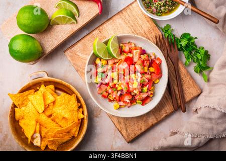 Frisch zubereiteter Pico de Gallo mit Mais und Limettenspaltern, serviert mit Tortillachips Stockfoto