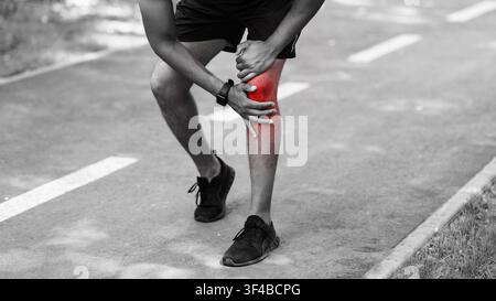 Nahaufnahme des jungen Sportlers, der Knieschmerzen auf der Joggingstrecke spürt, schwarz-weiß-Effekt Stockfoto