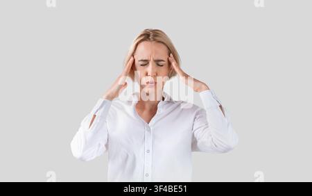 Überarbeiteter Büroangestellter, der unter starken Kopfschmerzen auf hellgrau leidet studio-Hintergrund Stockfoto