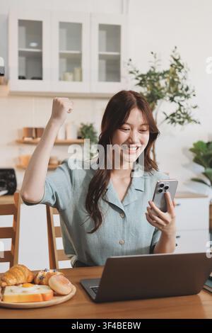 Glück Unternehmer schönes Geschäft asiatische junge Frau tragen lässig Handy zum Einkaufen online genießen Sie mit sozialen Medien und Laptop zu Hause Stockfoto