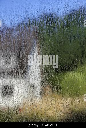 Regentropfen auf einer Fensterscheibe mit undeutlicher Sicht auf ein Haus mit Bäumen im Sommer, Witten, Nordrhein-Westfalen, Deutschland Stockfoto