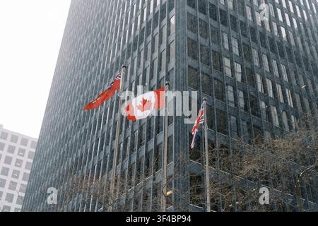 Das Staatssymbol weht vor dem Hintergrund einer urbanen Kulisse. Die Nationalflagge weht neben einem hoch aufragenden Wolkenkratzer mitten in einem winterlichen Land Stockfoto