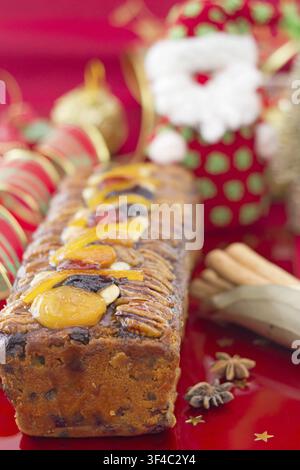 Weihnachtskuchen mit Früchten und festlicher Dekoration, vertikale Komposition, auf rotem Hintergrund Stockfoto