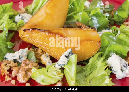 Salat mit karamellisierten Birnen, Walnüssen und Blauschimmelkäse auf rotem Teller Stockfoto