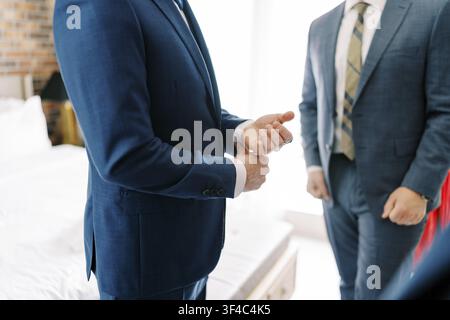 Zwei Führungskräfte in Marineblauen Anzügen, die sich während der Vertragsunterzeichnung in einem hellen modernen Büro die Hand geben, Nahaufnahme der verschränkten Hände Stockfoto