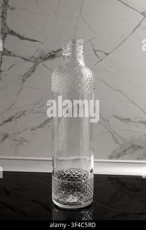 Leere klare Glasflasche mit strukturiertem Muster auf einem Marmorhintergrund. Minimalistische Küchenstilleben mit Platz für Text. Stockfoto