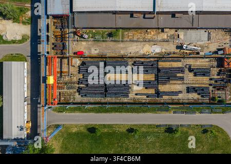 Luftbild eines industriellen Lagerhofs mit ordentlich gestapelten Metallrohren, einem großen Dachkran und umliegenden Betriebsgebäuden in K Stockfoto