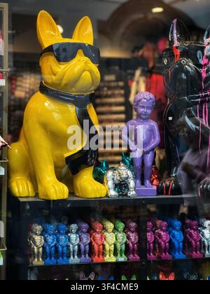 Farbenfrohe moderne Kunststatuen von Hunden und Figuren in einem Schaufenster. Eklektisches Schaufenster mit glänzenden gelben und schwarzen Bulldoggenstatuen, die tragen Stockfoto