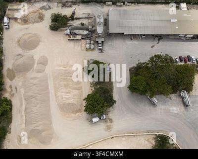 Luftaufnahme einer Ziegelwerkstatt mit großen Sand- und Kieshaufen, Industriesilos, einem Lagerhaus und geparkten Fahrzeugen in Mérida, Yucatán, Mexiko Stockfoto