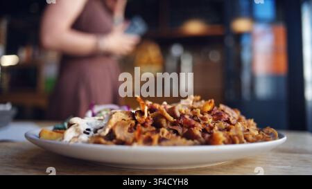 Großer Teller mit geschnittenem gegrilltem Kebab und Gemüse, Mädchen wählt Bestellung in der Nähe der Theke Stockfoto