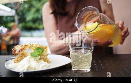 Mädchen gießt kalte Limonade in ein Glas in einem geschäftigen Sommercafé an einem beliebten Touristenort Stockfoto