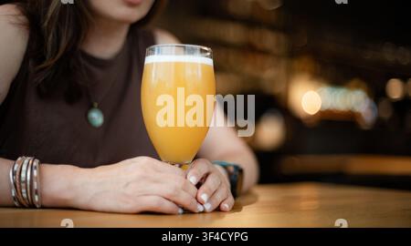 Frau genießt Weizenbier an einem Tisch in einem überfüllten Pub Stockfoto