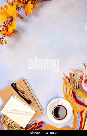 Gemütlicher Herbst-Arbeitsplatz mit einer heißen Kaffeetasse. Spiralnotizbücher. Lesebrille. Ein Stift. Und ein warmer, farbenfroher gestrickter Schal. Akzentuiert mit dekorativ Stockfoto