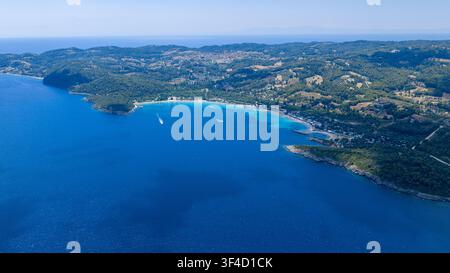 Eine hohe Luftaufnahme zeigt eine geschwungene blaue Bucht, einen hellen Strand und bewaldete Hügel, die mit Küstenhäusern gesprenkelt sind, in Golden Beach auf Kassandra in Chalkidiki, Griechenland. Stockfoto