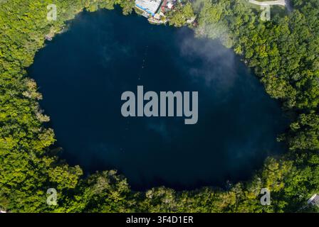 Luftaufnahme des Cenote Cocalitos mit seinem tiefen blauen Wasser, umgeben von dichtem grünem Dschungel in Bacalar, Quintana Roo, Mexiko. Stockfoto