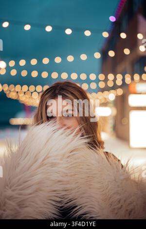 Frau steht in einem gemütlichen Bereich mit Lichterketten bei Nacht, während sie ihr Gesicht teilweise verdeckt Stockfoto