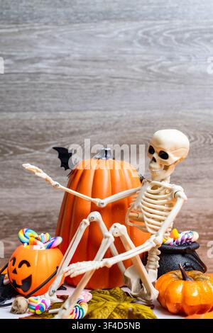 Halloween-Dekorationen zeigen ein Skelett, Kürbisse, Süßigkeiten und eine Fledermaus vor einem Holzhintergrund Stockfoto