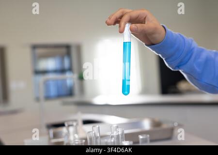 Afroamerikanischer Teenager in hellblauer Bluse hält ein mit hellblauer Flüssigkeit gefülltes Reagenzglas im Labor Stockfoto