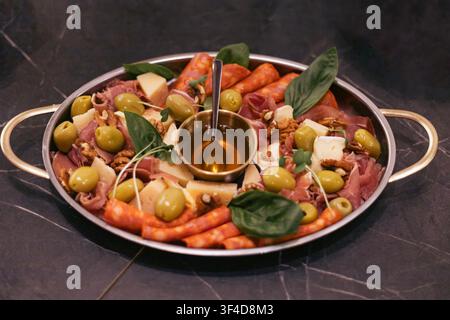 Ein Metalltablett mit verschiedenen Prosciutto, Salami, grünen Oliven, verschiedenen Käsesorten, Nüssen und Basilikumblättern sowie einer kleinen Schüssel Honig in der Mitte und einem Stockfoto