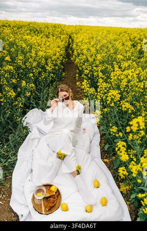 Frau genießt ein Picknick in einem lebhaften gelben Rapsfeld an einem sonnigen Tag Stockfoto