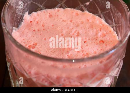 Ein cremiger rosa Erdbeer-Milchshake mit Schaumhaube in einem strukturierten Glas, schaumiger, blubbernder Oberfläche und weicher Pastellfarbe, die süße, erfrischende Vergnüglichkeit vermittelt Stockfoto