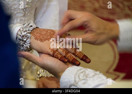 Nahaufnahme eines Bräutigams, der der Braut einen goldenen Ehering an den Finger steckt, verziert mit aufwendigen Henna- (Mehndi-)Mustern und einem Diamantarmband während einer traditionellen Hochzeitszeremonie. Stockfoto