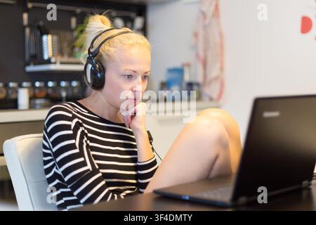 Frau in den casual home Kleidung Arbeiten und Studieren aus der Ferne von ihrer kleinen Wohnung spät in der Nacht. Home Küche im Hintergrund. Große Flexibilität von web-basierten Kurse und Studiengänge. Stockfoto