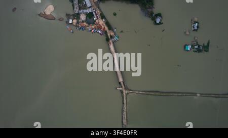 Kishoreganj, Bangladesch - 13. Oktober 2024: Luftaufnahme von Nikli Haor, die eine schmale Straße zeigt, die das Wasser überquert, kleine Boote, die am Ufer festgemacht sind, und Sca Stockfoto
