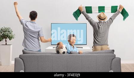 Junge mit Vater und Großvater, die ein Fußballspiel im Fernsehen anfeuern und beobachten Stockfoto