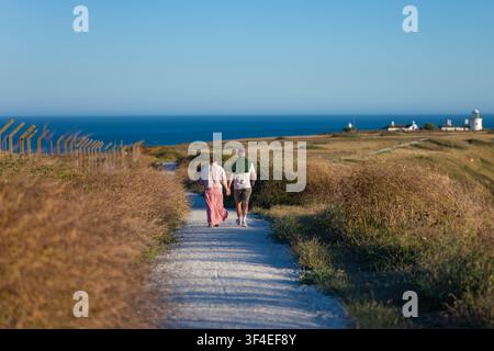 Paar, das Händchen haltend, geht einen Kreideweg entlang in Richtung Belle Tout Leuchtturm auf dem South Downs Küstenweg in East Sussex Stockfoto