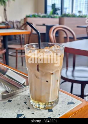 Nahaufnahme eines erfrischenden Eiskaffee-Lattes in einem hohen Glas mit einem schwarzen Strohhalm auf einem gesprenkelten Terrazzotisch in einem modernen Café. Stockfoto