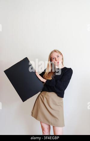 Lächelnde junge Frau hält ein leeres schwarzes Präsentationsbrett, perfekt für Werbung, Branding, Marketing oder Werbe-Mockup. Stockfoto