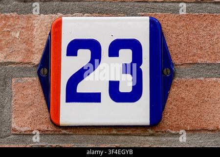 Ansicht eines Hausnummerschilds mit der Nummer 23, das an einer Ziegelwand in Baarle-Nassau, Nordbrabant, Niederlande, angebracht ist. Stockfoto