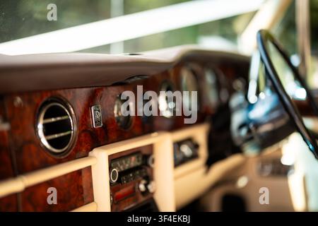 Nahaufnahme eines klassischen Rolls-Royce-Armaturenbretts, das Walnuss-Splintholzfurnier, verchromte Lüftungsschlitze, Anzeigen und das RR-Emblem zeigt. Stockfoto