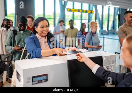 Frau, die sich an einem belebten Flughafenschalter anmeldet Stockfoto