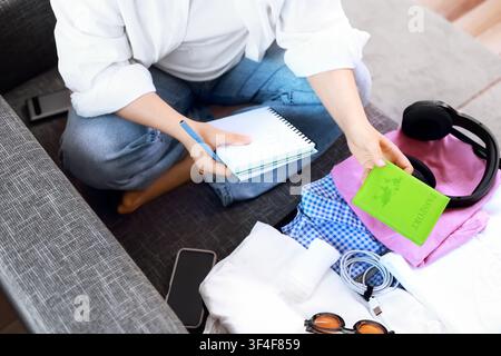 Frau hält einen Pass und eine Packliste während der Reisevorbereitung. Sie bereitet ihr Gepäck und ihren Koffer für eine Sommerurlaubsreise vor mit Stockfoto