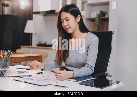 Junge asiatische Geschäftsfrau lächelt und arbeitet an einem Laptop, während sie an ihrem Schreibtisch in einem modernen Büro sitzt Stockfoto
