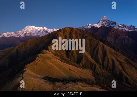 Luftbild des majestätischen Machapuchare-Gipfels und der umliegenden Annapurna-Bergkette zur goldenen Stunde, mit grasbewachsenen Graten und schneebedeckten Gipfeln Stockfoto