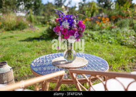 Nahaufnahme eines Blumenarrangements, das auf einem Glastisch im Sommergarten steht. Lounge-Bereich mit Möbeln und Strauß frischer Blumen in einer Vase Stockfoto
