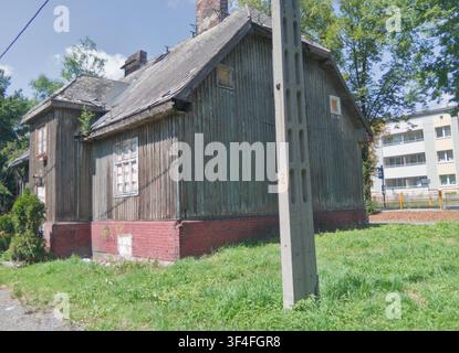 ŚWIĘTOCHŁOWICE, SCHLESIEN, POLEN – 28. JULI 2026: Ein leerstehendes Holzarbeiterhaus von 1934 steht neben einem modernen Wohnblock in der Chorzowska-Straße im Piaśniki-Viertel von Świętochłowice. Der Blick kontrastiert das verwitterte Holzgebäude und seinen rotbacksteinernen Sockel mit der neueren städtischen Bebauung in der Nähe. Es ist eines von fünf kommunal gelisteten Häusern, die lokal als domki fińskie bekannt sind und die noch nicht verkauft wurden, was die Spannungen zwischen dem Erhalt historischer Arbeiterwohnungen und der Sanierung in einer sich wandelnden Stadt in Oberschlesien verdeutlicht. Stockfoto