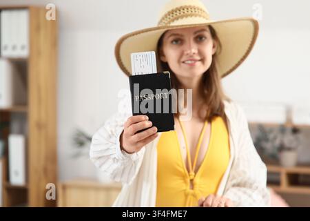 Junge Frau mit Strohhut und gelbem Badeanzug, die einen Pass und eine Bordkarte hält, bereit für den Sommerurlaub und die Ferien Stockfoto