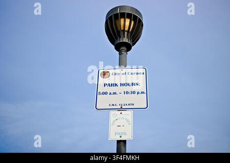 Stadt-Corona-Parköffnungszeiten-Schild, das an einem Laternenpfahl montiert ist, vor einem klaren blauen Himmel in einer öffentlichen Parkanlage in Corona, Kalifornien. Stockfoto
