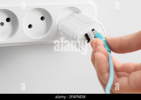 Hand, die ein blaues USB-Kabel in einen weißen Dual-Port-USB-Wandladeadapter in einer Steckdosenleiste steckt, der Ladeadapter ist in eine weiße Steckdosenleiste eingesteckt, Pro Stockfoto