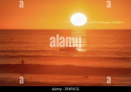 Silhouette eines Fischerboots auf goldenem Ozean bei Sonnenuntergang, zeigt warmes Abendlicht, ruhige See und eine friedliche Küstenlandschaft. Stockfoto